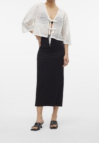 Witte gehaakte crop top met een strik aan de voorkant, gecombineerd met een zwarte, getailleerde, knielange rok en zwarte open-toe mules.