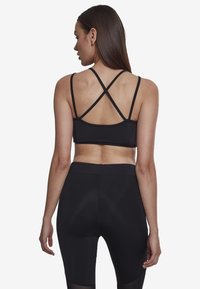 Črn športni modrček s križnimi naramnicami, izdelan iz elastičnega materiala. Nosi se z ujemajočimi črnimi visokimi leginami. Gladka tekstura.