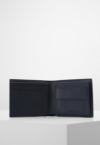 Tamsiai mėlynas odinis piniginė su keliais kortelių kišenėmis ir skyriumi. Lygus paviršius, minimalistinis dizainas, su išstumtu logotipo detalizavimu.