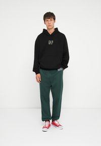 Black hoodie with "GAP" logo, green sweatpants with logo detail, and red sneakers. Smooth texture, casual design.