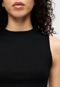 Μαύρο αμάνικο τοπ με στρογγυλή λαιμόκοψη. Λείο, ελαστικό ύφασμα με εφαρμοστή γραμμή, που αναδεικνύει μια διακριτική υφή.