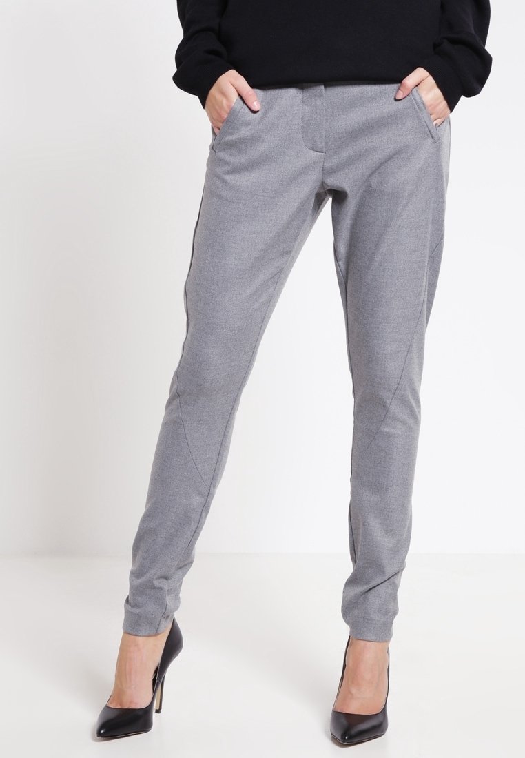Šedé kalhoty na míru s hladkou texturou, bočními kapsami a slim fit. V páru s černými vysokými podpatky vytvářejí formální vzhled.