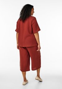 Haut ample de couleur rouille, texturé, à manches courtes, associé à un pantalon cropped assorti. Design simple sans motifs visibles.