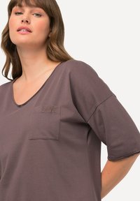 Kortærmet, mauve t-shirt lavet af blødt stof med V-hals og en lomme, der har "LOVE" broderet med matchende tråd.