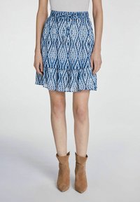 Mini-jupe bleue à motifs avec un ourlet volanté et une taille à cordon, fabriquée en tissu léger. Associée à des bottines beiges.