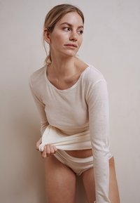 Langærmet cremetop og matchende undertøj, lavet af blødt stof med en glat tekstur. Toppen har en rund halsudskæring og tætsiddende ærmer.