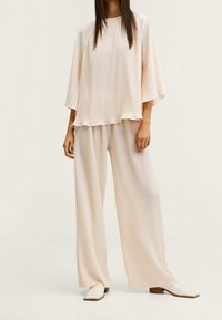 Jasnobeżowa, żeberkowana bluzka z szerokimi rękawami, w zestawie z luźnymi, dopasowanymi spodniami. Charakteryzuje się miękką teksturą i swobodnym krojem. Buty o kwadratowych noskach.