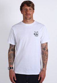 T-shirt blanc à col rond avec un graphique bleu d'un homme surfant sur la poitrine gauche. Manches courtes, en coton, coupe décontractée.