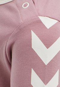 Lyserødt stof med en ribbet tekstur, der har store hvide chevron-mønstre. Inkluderer en lille hvid trykknapdetalje.