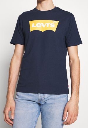 Námořnická modrá polokošile s krátkým rukávem vyrobená z bavlny, s velkým žlutým logem Levi's na hrudi. Volný střih s kulatým výstřihem.
