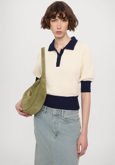 Haut polo en tricot crème avec col marine, manches courtes et poignets côtelés. Jupe en denim bleu clair, portant un sac à main en suède vert.