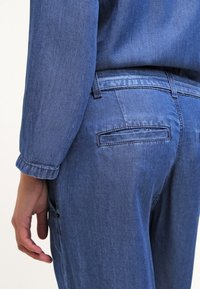 Džínové kalhoty ve středně modré barvě, bezšvovým zadním kapsou, rovný střih a měkkou texturou. Rukávy mají detail manžety.