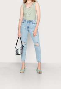 Lys grøn, ærmeløs bodysuit med blomstermønster, parret med lyseblå, slidte high-waisted jeans, grønne block-heeled sandaler og en stribet håndtaske.