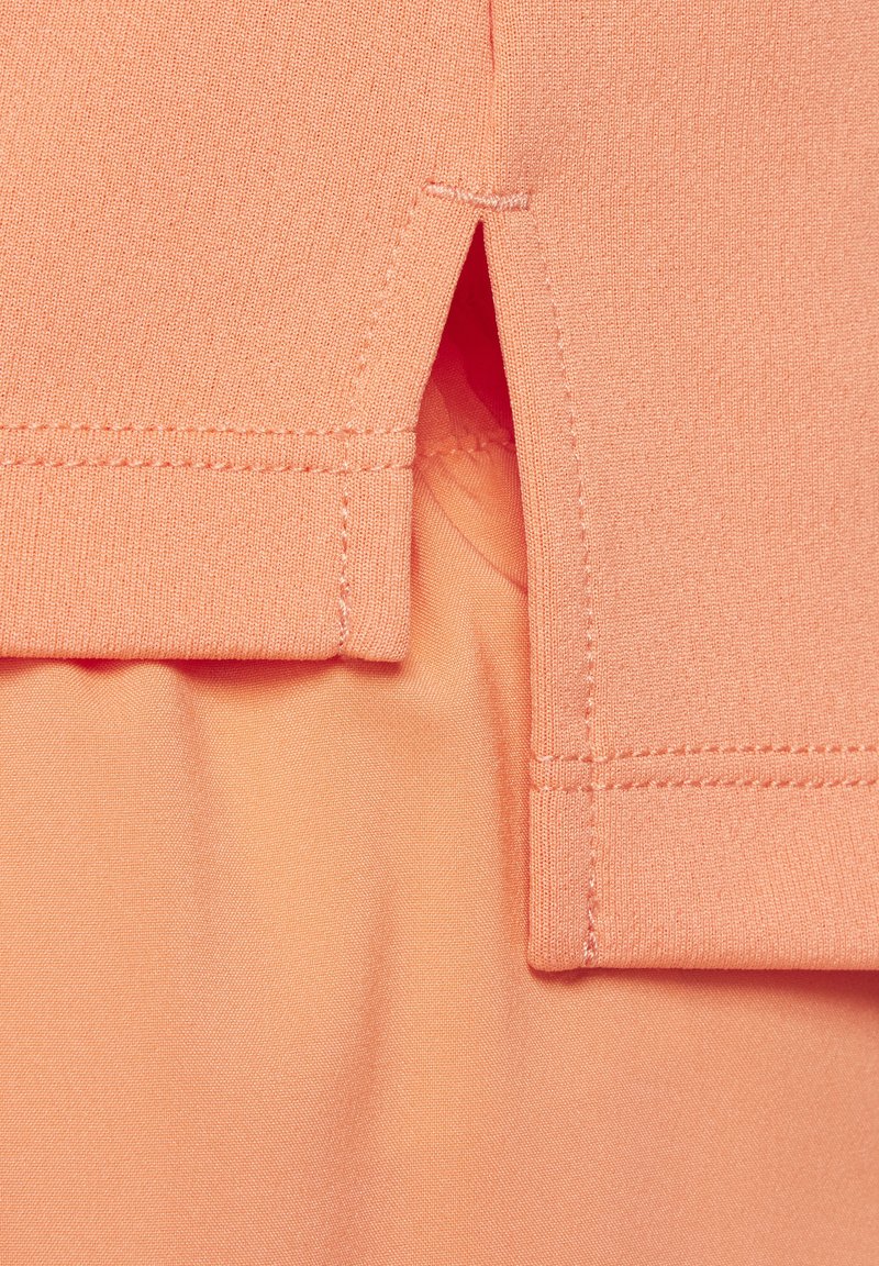 Pfirsichfarbener Stoff mit glatter Textur, versehen mit einem seitlichen Schlitz und Akzentnähten. Das Design umfasst geschichtete Stoffelemente.