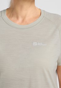 T-shirt grigio chiaro, maniche corte, scollatura rotonda, texture liscia, con piccolo logo bianco sul petto, cuciture lungo le cuciture.