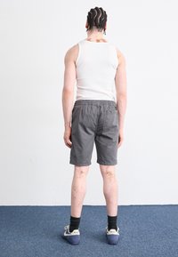 Shorts en coton gris avec taille élastique, une poche arrière et des ourlets roulés, associés à un débardeur blanc et des chaussettes noires.