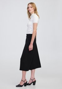 Top blanco de manga corta combinado con una falda negra de cintura alta. La falda tiene un diseño fluido. Zapatos de tacón negros con correas en el tobillo.