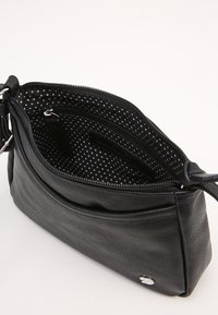 Černá kožená taška přes rameno s hlavním oddílem na zip, šedou podšívkou s puntíky a vnitřní kapsou na zip.