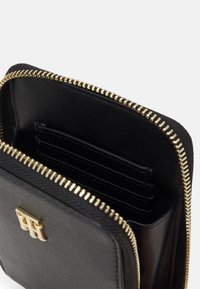 Musta nahkainen lompakko, jossa on kullanvärinen vetoketju, useita korttipaikkoja ja teksturoidulla pinnalla oleva logo edessä.