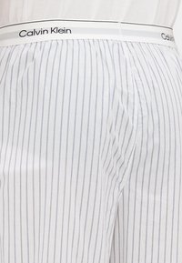 Calvin Klein svītrainas pidžamas šortus ar balto bāzi un gaiši ziliem vertikāliem svītrām. Tiem ir elastīga jostasvieta ar logo.