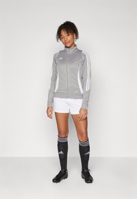Gray athletic jacket with white accents, zip front, and logo; paired with white shorts and black socks featuring white stripes and logo.
