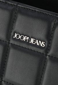 Črna prešita usnjena torba z metalno srebrnim logotipom "JOOP! JEANS", z drobnim šivom in teksturirano površino.