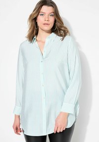 Camisa de manga larga a rayas azul claro con cuello abotonado, que presenta botones blancos y aberturas laterales en el dobladillo. La tela parece suave.