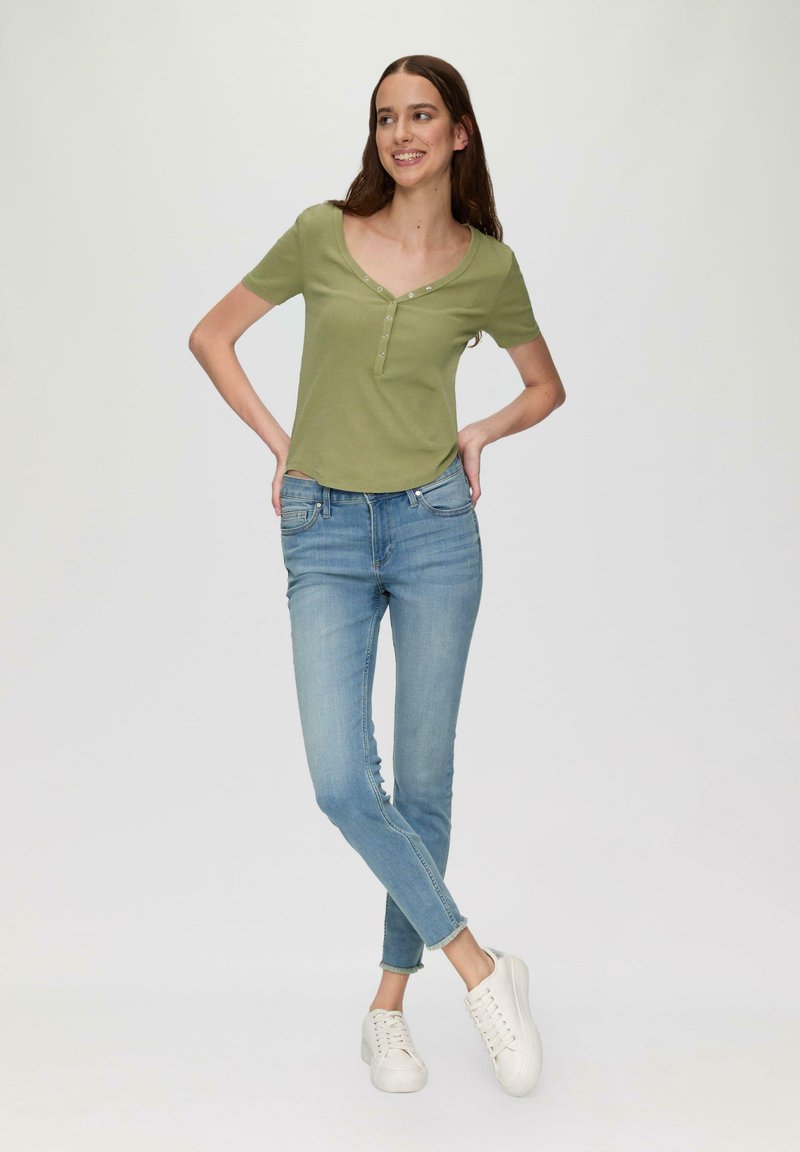 Groene korte mouwen top met een V-hals en knoopdetail, gecombineerd met lichtblauwe jeans en witte sneakers. Eenvoudig, casual outfit ontwerp.