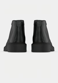 Černé kotníkové boty s hladkým koženým svrškem, nízkým blokovým podpatkem a kontrastní černou gumovou podrážkou. Obsahují jemné detaily šití.