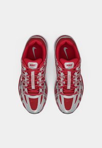 Červené a strieborné topánky Nike s priedušným zvrškom, podrobným šnurovaním a výrazným logom. Dizajn obsahuje textúrované vzory a akcenty.