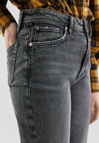 Czarne, wysoka talia dżinsy wykonane z denimu z lekkim streczem. Cechy to miedziane nity, pięć kieszeni oraz lekko wyblakła tekstura.