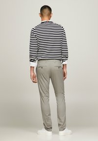 Camicia a maniche lunghe a righe in blu navy e bianco con polsini arrotolati, abbinata a pantaloni grigi chiari e sneakers bianche. Vista posteriore mostrata.