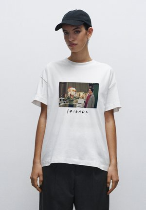 Person wearing white t-shirt with "Friends" TV show scene showing a woman in a chicken costume talking to a man in a kitchen.