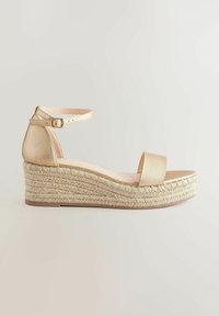 Sandale à talon compensé couleur or avec une tige en cuir texturé, une bride ajustable à la cheville, et une semelle en jute avec une plateforme, dotée d'une semelle intérieure plate.