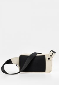 Crossbody tas met een gestructureerde zwarte gaaszijde, gladde crème materiaal, verstelbare schouderriem en knoopaccenten op de sluiting.