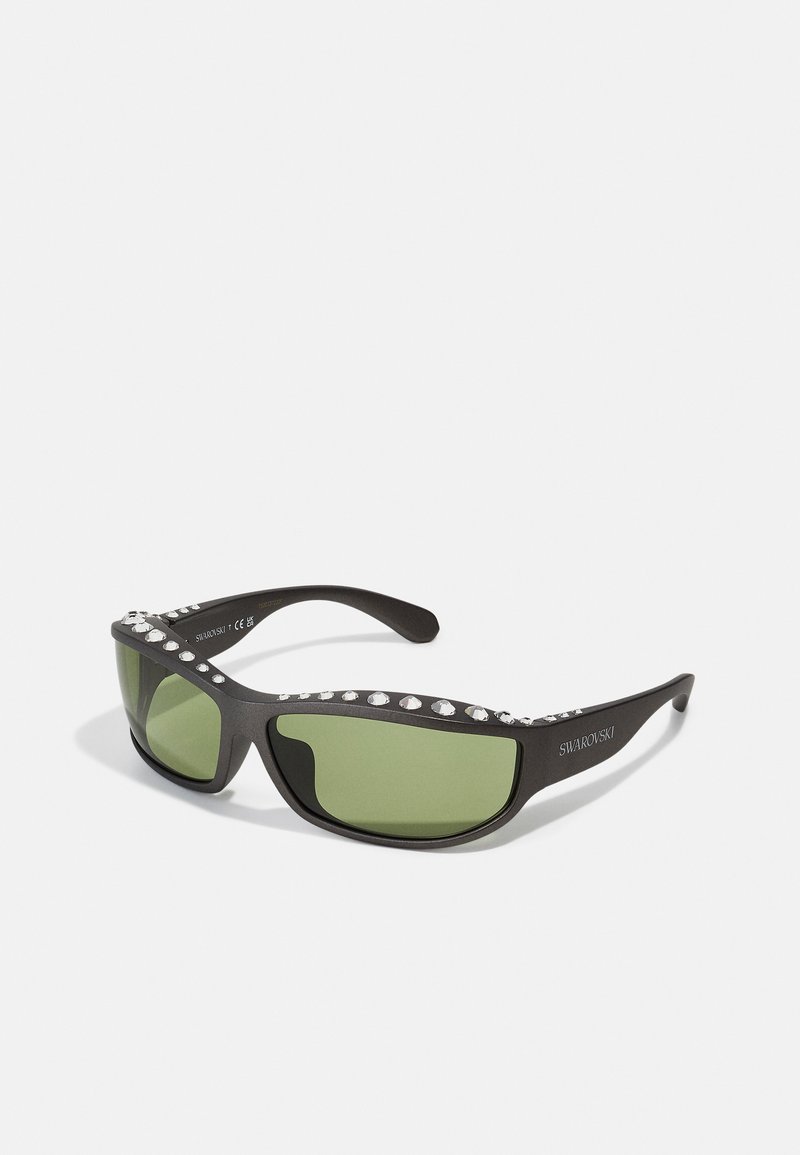 Černé sluneční brýle se zelenými skly, zdobené čirými krystaly podél horní hrany rámečku. Elegatní design a sportovní tvar.