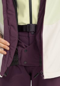 Lila und cremefarbene Skijacke mit Reißverschluss, verstellbarem Bund und Taschendetails. Hergestellt aus langlebigem, wetterfestem Material.