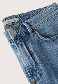 Vaqueros de mezclilla azul claro con un corte holgado, que cuentan con un botón metálico, cremallera y costuras en contraste de color amarillo a lo largo de las costuras y los bolsillos.