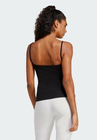 Čierny rebrovaný top s tenkými ramienkami, ktorý ukazuje priliehavý siluetu a hladkú textúru, skombinovaný s bielymi legínami na neutrálnom pozadí.