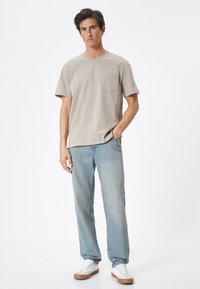 Lys grå bomulds T-shirt med en brystlomme, parret med lyseblå denim jeans og hvide sneakers med en brun gummisål.