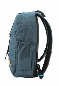 Mochila de tela en color verde azulado con correas de malla negra acolchadas, bolsillo lateral elástico, asa superior de transporte y un pequeño parche de logo en la parte frontal.