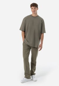 Oversized olive green t-shirt with a round neckline, paired with matching relaxed-fit olive green pants and white sneakers.