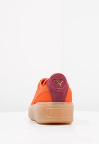 Baskets en suede orange avec une semelle transparente épaisse, dotées d'une languette de talon violet foncé et de détails de logo doré à l'arrière.