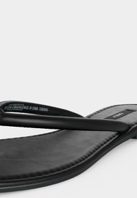 Μαύρο επίπεδο σανδάλι με ελάχιστα λουράκια, επενδεδυμένο πέλμα και ετικέτα μάρκας "ONLY" στην περιοχή της φτέρνας.