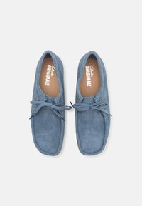 Blauwe suede loafers met een zachte textuur, voorzien van een ronde neus en een strikdetail aan de voorkant. De binnenvoering toont het merk "Clarks ORIGINALS".