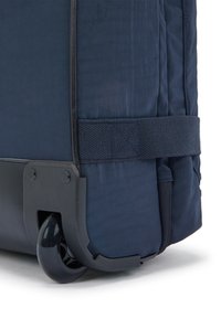 Ingrandimento dell'angolo di una valigia blu navy con ruote, che mostra la texture del tessuto, la cinghia rinforzata e la ruota in plastica nera con custodia protettiva.