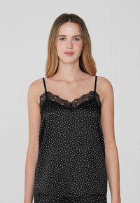 Camiseta de satén negra con lunares blancos, con tirantes finos y un borde de encaje en el escote. Textura suave y corte holgado.