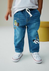 Vaaleansiniset farkkuhousut, joissa on kirjailtuja traktori- ja lehmämalleja, rento istuvuus ja säädettävä kiristysnauha vyötäröllä.