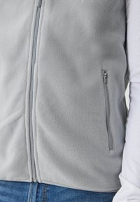Vest gri din fleece cu fermoar frontal și o buzunar lateral. Textura este moale, având un finisaj neted și cusături subtile.