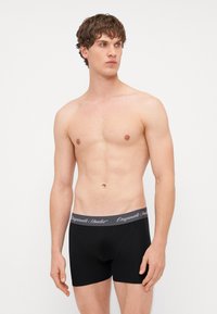 Boxer-briefs noirs avec une ceinture élastique grise comportant "Originals Studio" en cursive. Le tissu a une texture lisse.